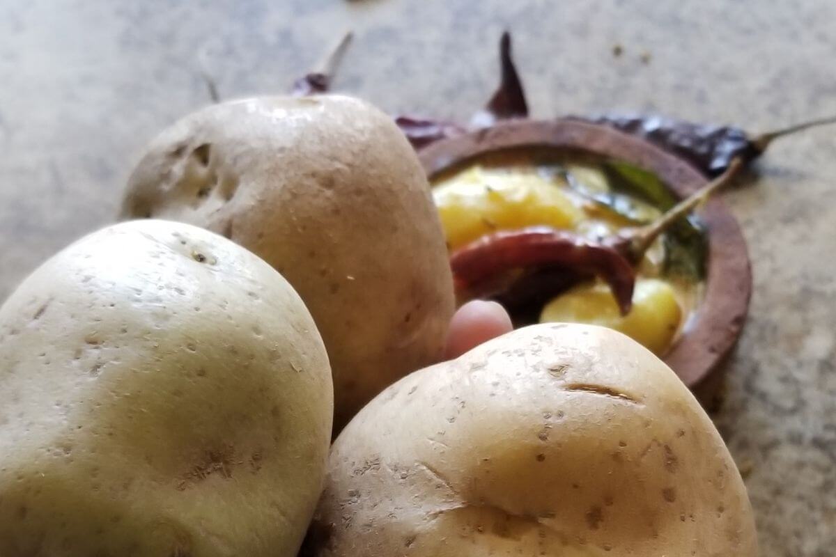 close up of the potatoes and further back a Clay pot filled with Sri Lankan potato curry ready to serve.