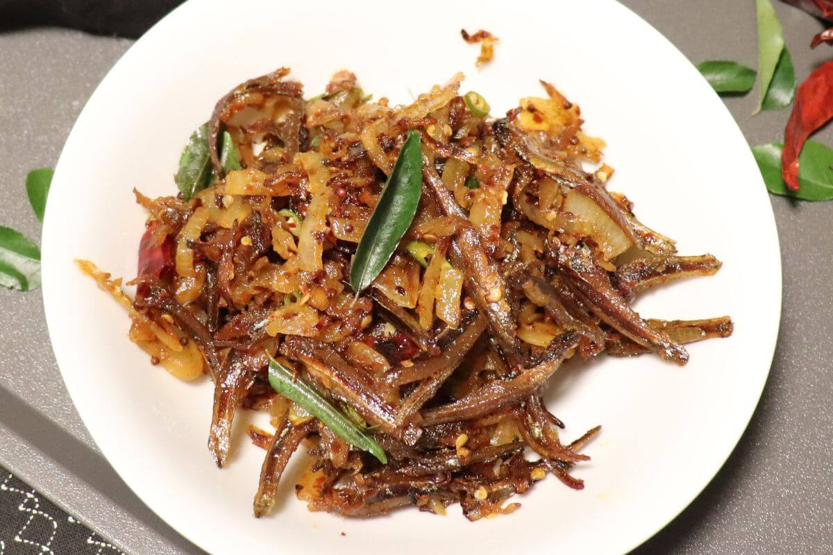 Close-up of crispy fried anchovies coated in spicy sambal with onions and chili.