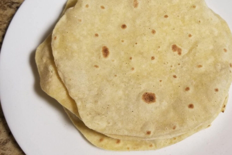 Freshly made chapati stacked on a plate, soft and warm with golden brown spots.