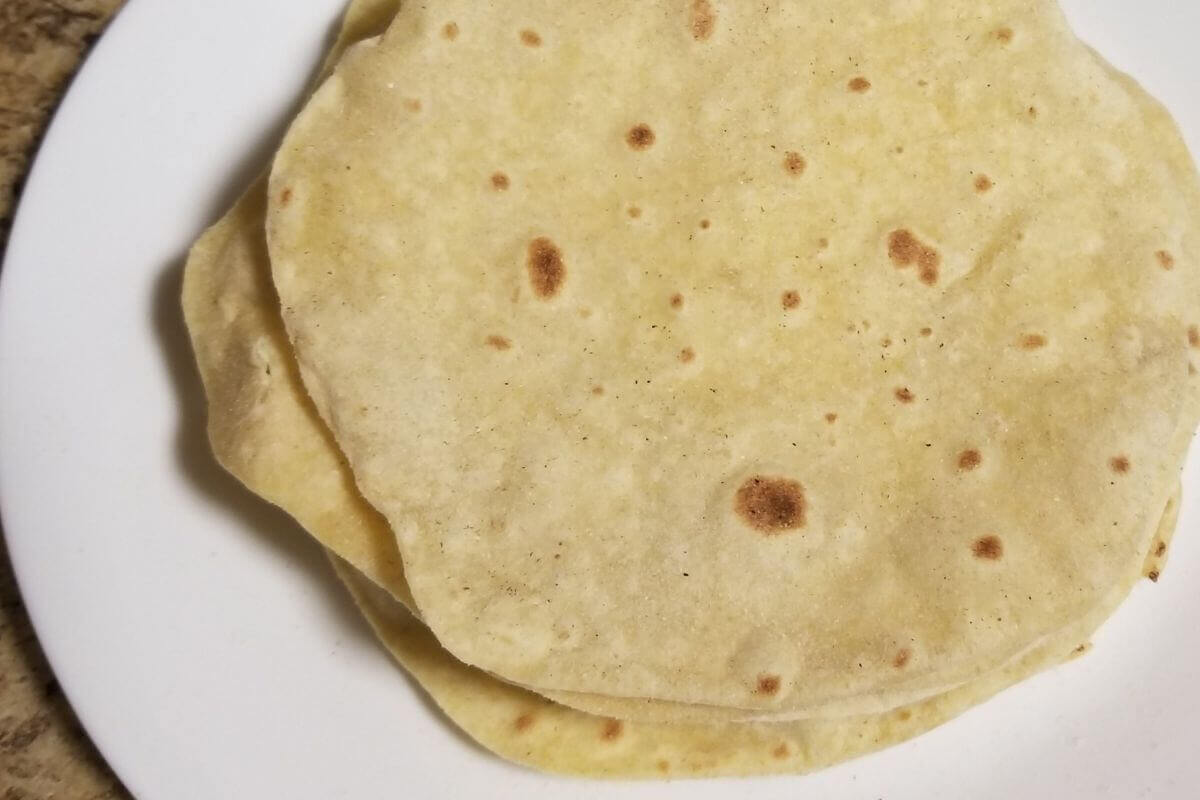 Freshly made chapati stacked on a plate, soft and warm with golden brown spots.