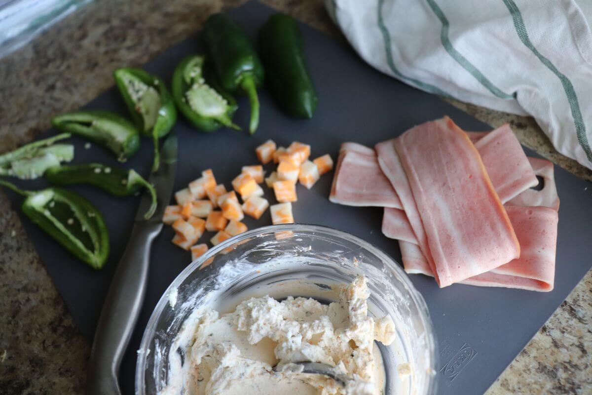 Ingredients for chicken‑wrapped jalapeño poppers, including jalapeños, cheese, and chicken strips arranged on a board.