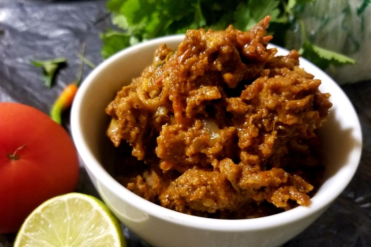 Side view of dry‑style meat curry showing its thick masala and tender texture.  