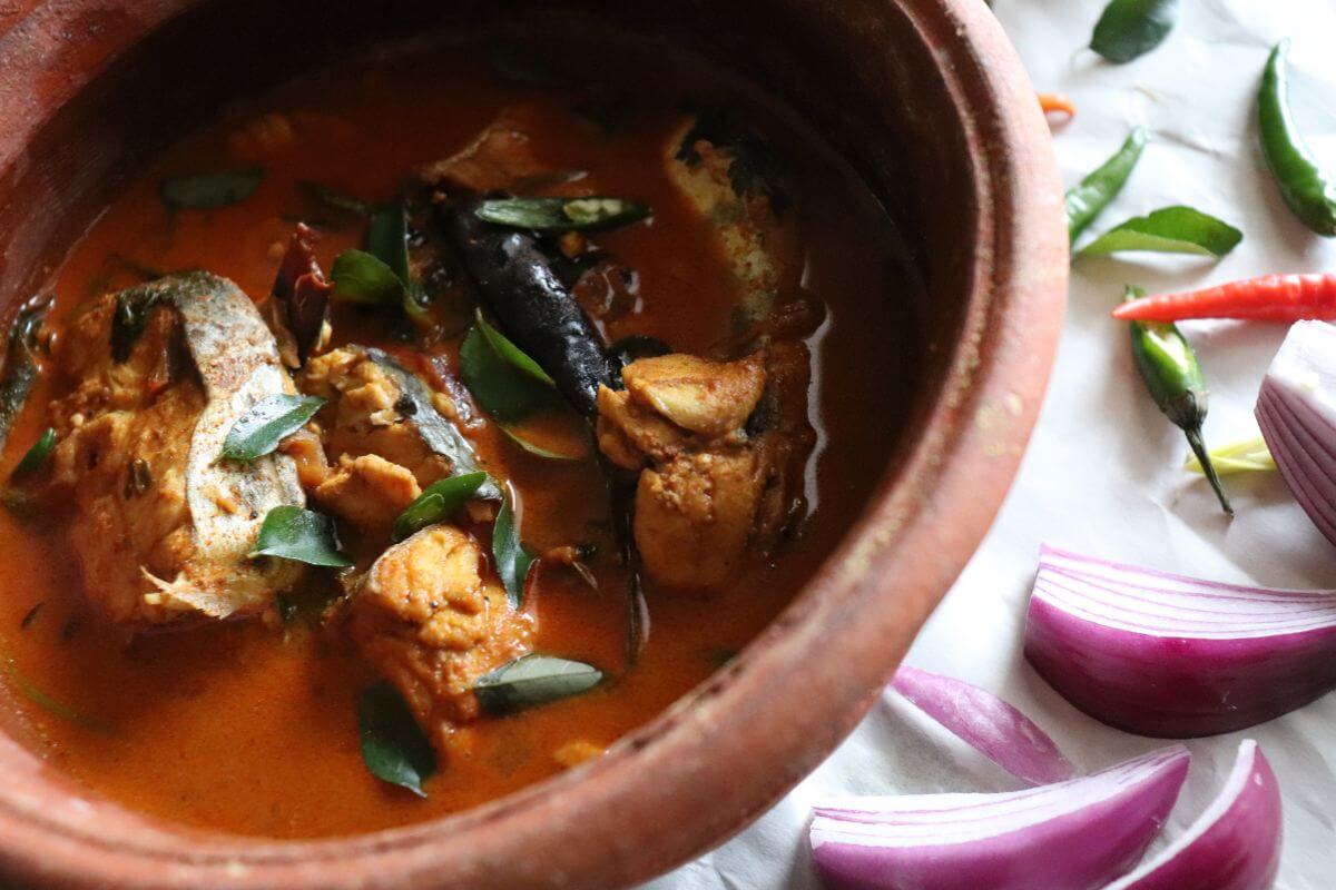 Fish curry simmering in a pot with coconut milk, spices, and curry leaves.