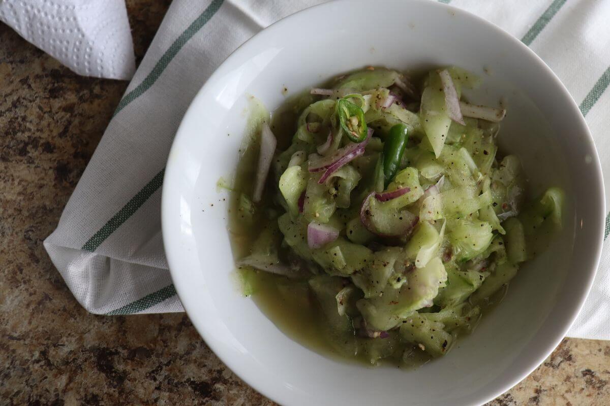 Overhead view of Sri Lankan cucumber salad in a white bowl, ready to serve as a fresh, vegan side dish.