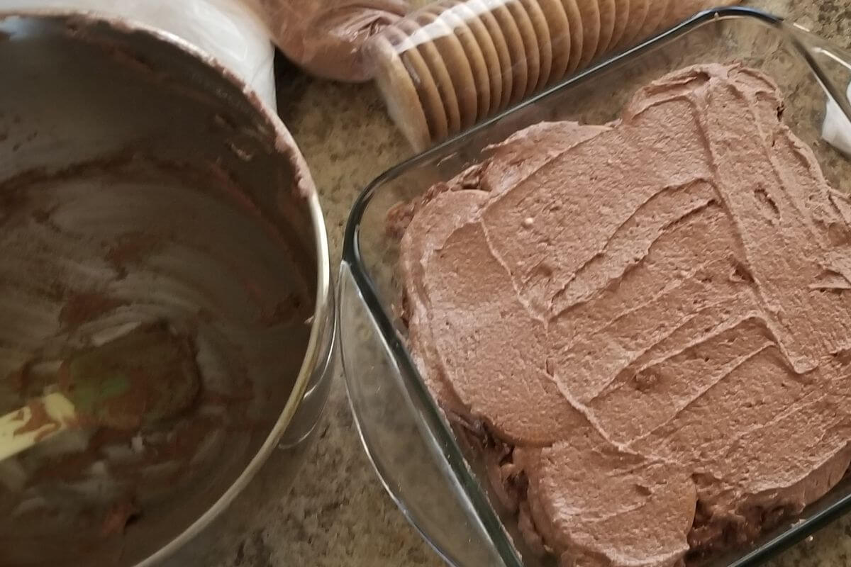 messy table with Sri Lankan chocolate biscuit pudding dessert layered with an empty bowl of buttercream on the side