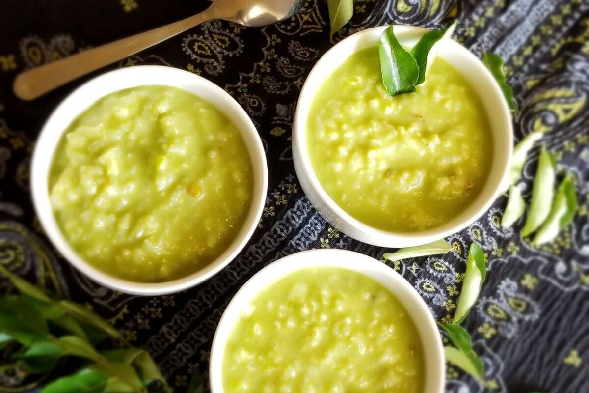 Green herbal porridge (Gotu Kola Kanda) served in a white bowl with fresh curry leaves around it.