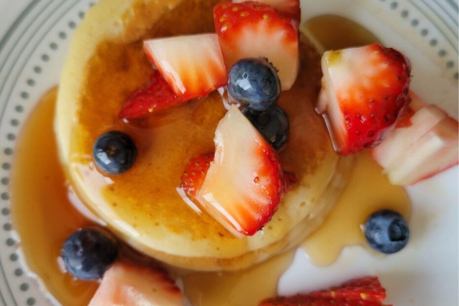 few pancakes placed on a plate, topped with berries and pancake syrup already poured ready to eat