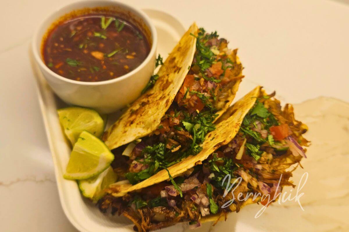Crispy birria tacos dipped into red consommé with melted cheese, cilantro, onion, and lime on the side.