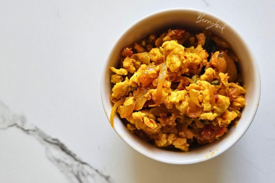 Close-up of spiced scrambled egg sambal with onions and chilies in a white bowl.