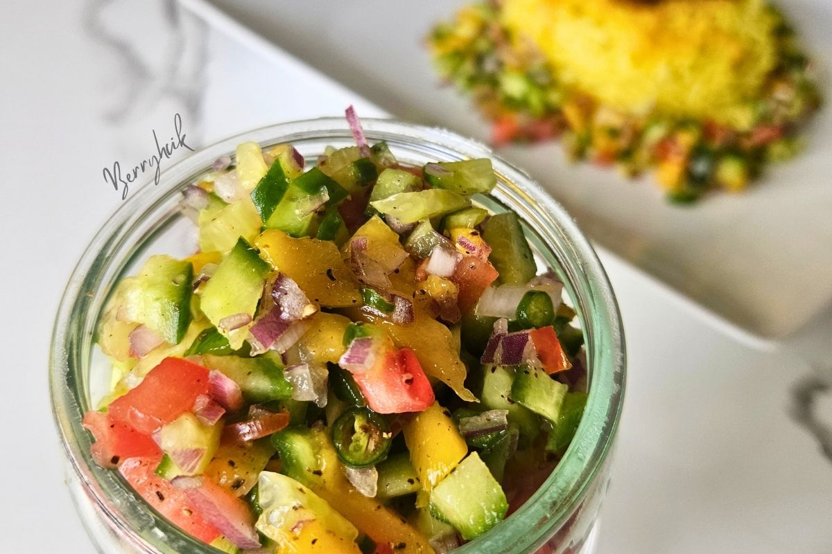 Fresh cucumber pineapple salad in a glass jar with diced tomatoes, onions, chilies, and peppers.