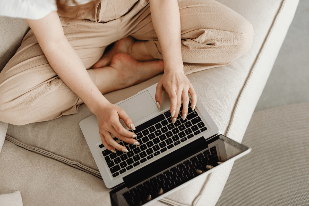 Person sitting cross‑legged on a sofa typing on a laptop while drafting a recipe blog post