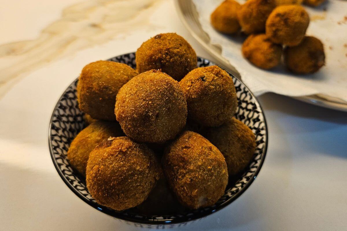 a bowl full of sri lankan fish cutlets piled next to a plate of more fish cutlets fresh off the fryer