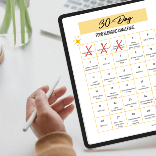 A person marking off completed days on a digital 30‑day food blogging challenge calendar displayed on a tablet beside a cup of coffee.